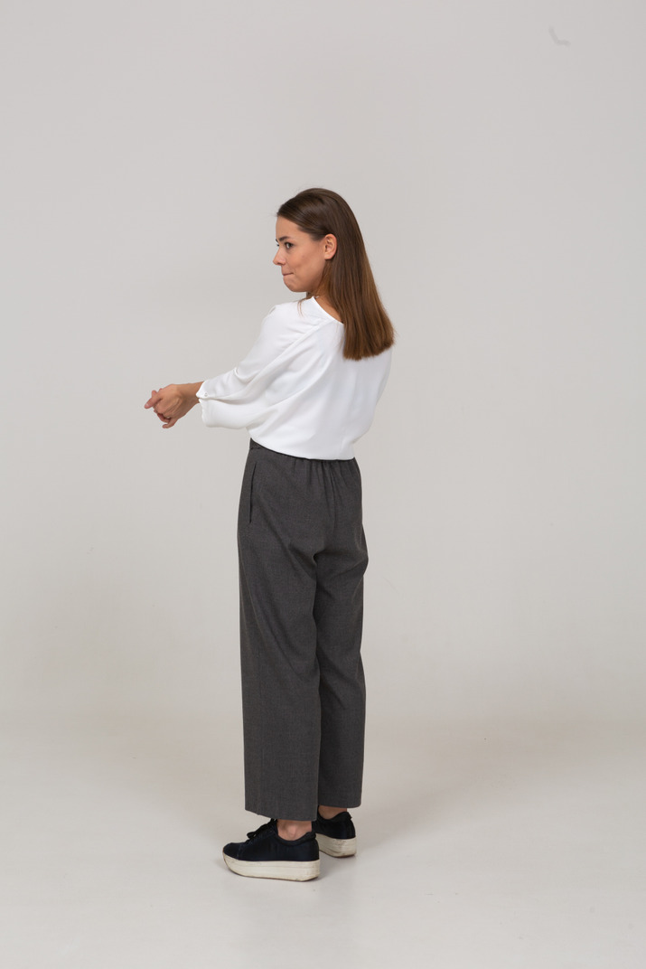 Three-quarter back view of a young lady in office clothing pressing lips and outstretching arms