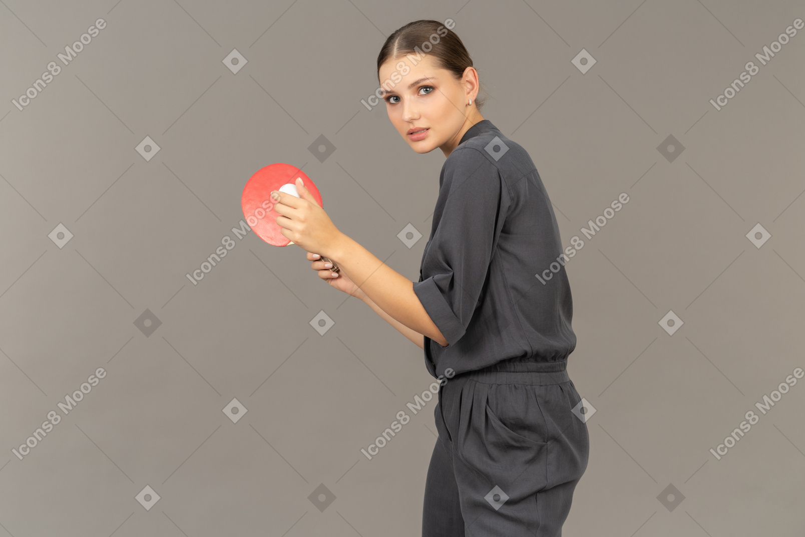 Side view of young woman in a jumpsuit serving tennis ball