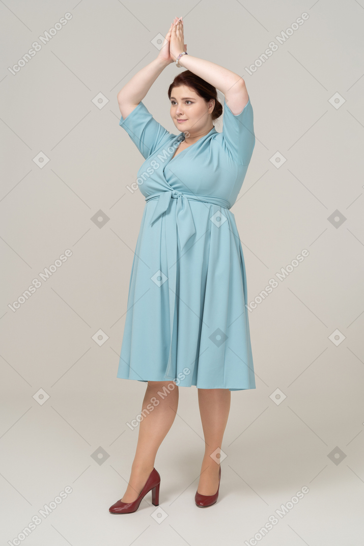 Front view of a woman in blue dress posing with hands over head