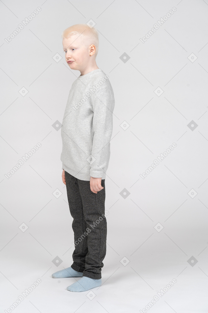 Puzzled kid boy standing still in grey sweater screwing lips