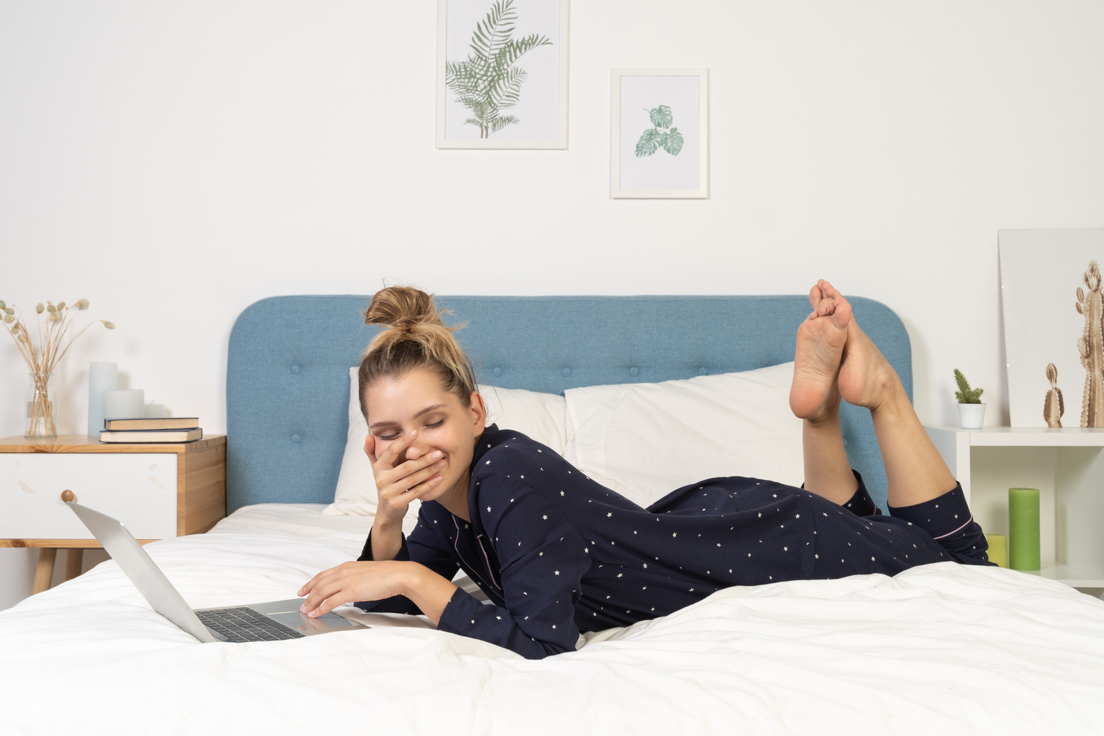 Side view of a smiling young female laying in bed with her laptop