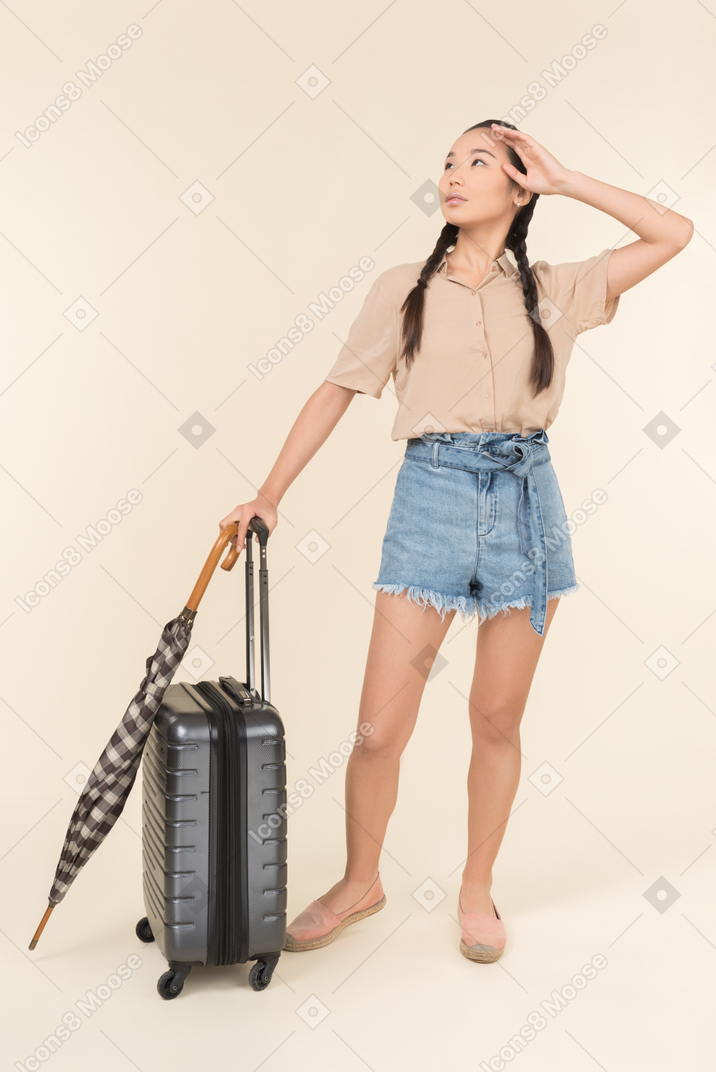 空を見てスーツケースと傘を持つ若い女性
