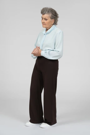 Three-quarter view of an old woman clasping hands sadly