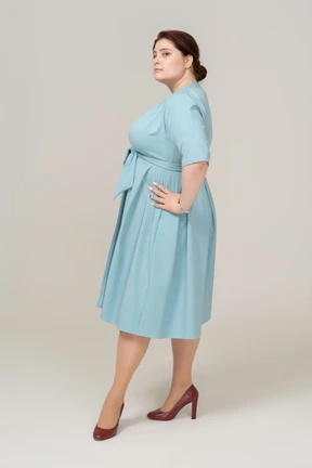 Side view of a woman in blue dress posing with hands on hips
