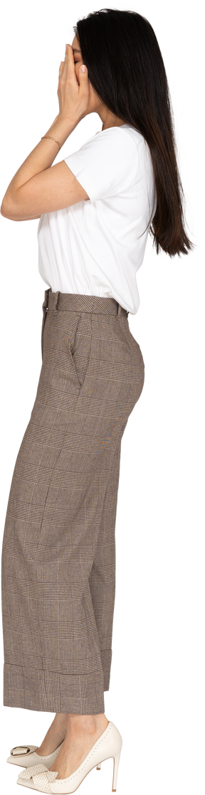 Vista lateral de uma jovem de calça e camiseta escondendo o rosto