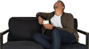 Front view of a smiling young man sitting on a sofa with a cup of coffee