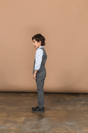 Vista laterale di un ragazzo carino in abito grigio che mostra la lingua