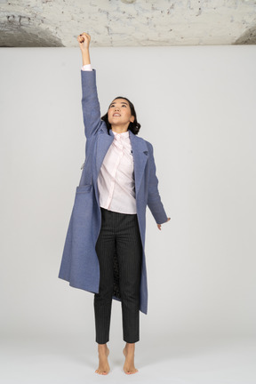 Excited woman in coat stretching hand up