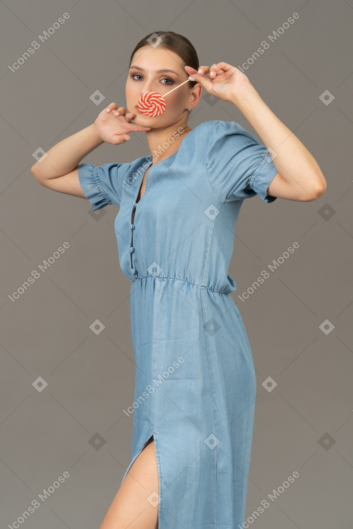 Three-quarter view of a young woman in blue dress holding a lollipop