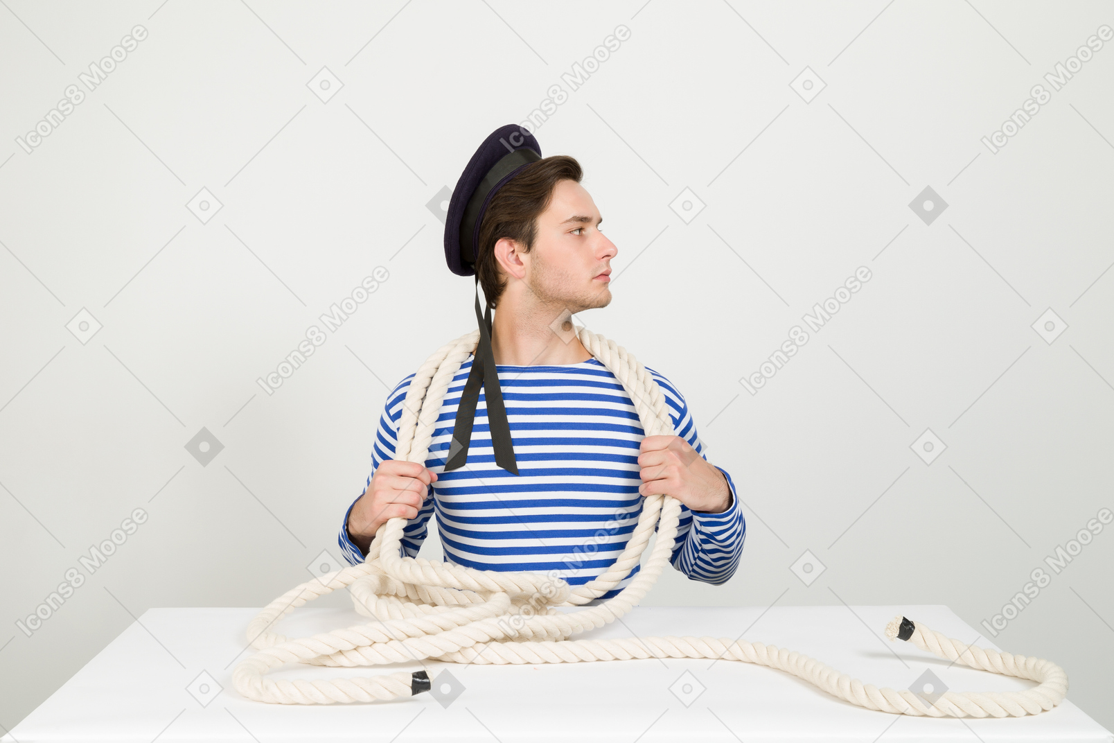 Sailor sitting at the table with marine rope on his neck and looking aside