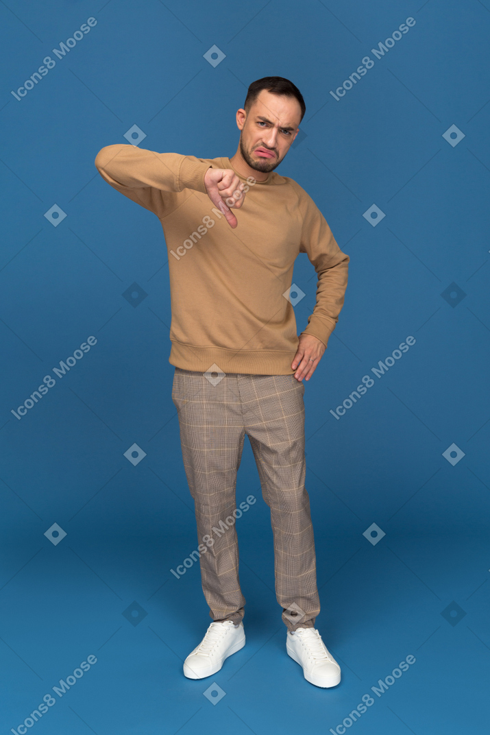 Young man showing thumb down and grimacing