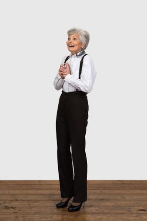 Vue des trois quarts d'une vieille femme surprise habillée en vêtements de bureau mettant les mains ensemble