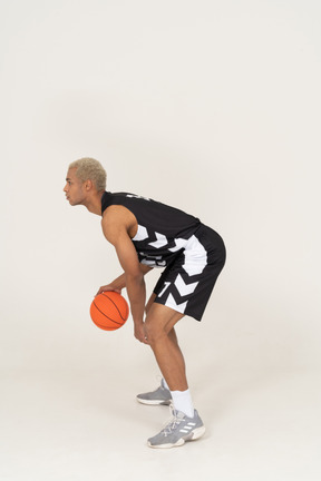 Vista lateral de um jovem jogador de basquete fazendo dribles