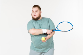 Großer kerl in der sportkleidung, die tennisschläger und tennisball hält