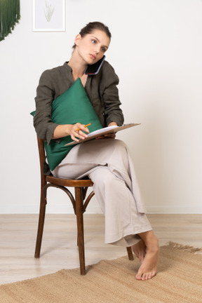 Front view of a young woman sitting on a chair with a tablet and having a phone call