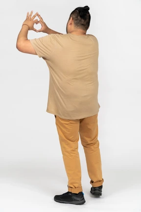 Brunette asian man making heart gesture with both hands back to camera