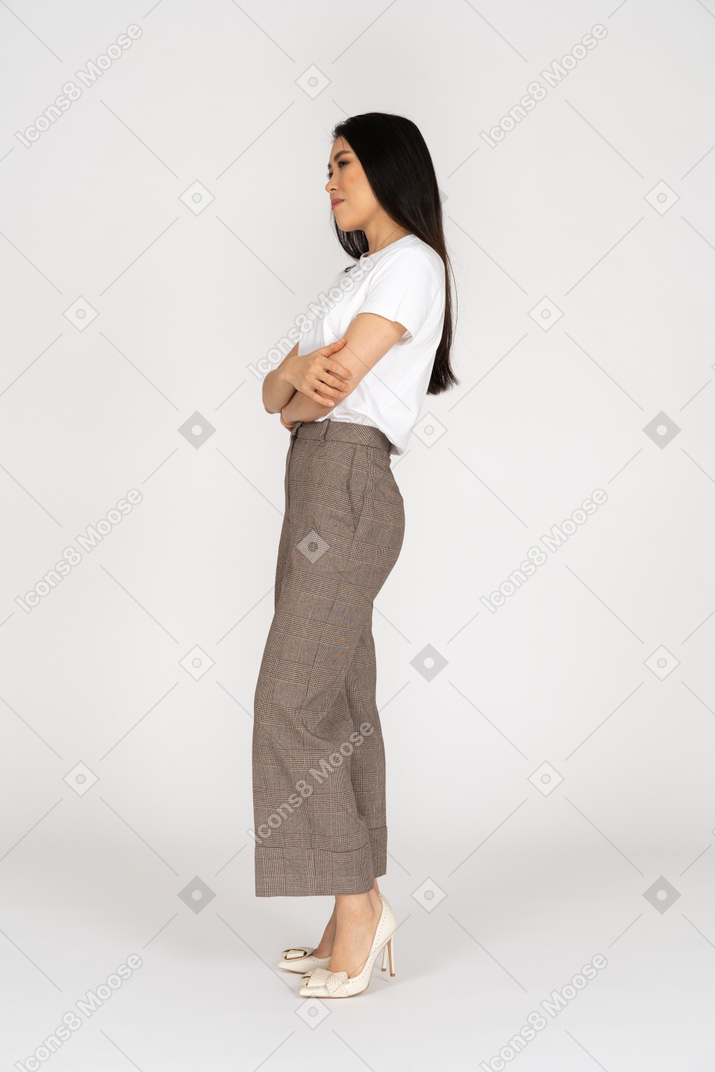 Vista laterale di una giovane donna sospettosa in calzoni e t-shirt attraversando le mani