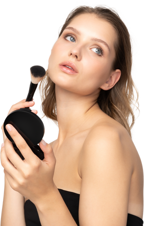 Side view of a young woman applying face powder while holding a mirror