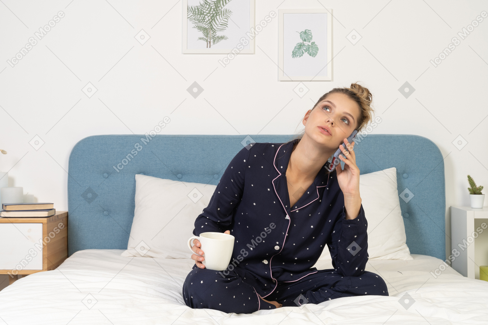 Front of a young female in pajama sitting in bed holding the cup and having a phone call