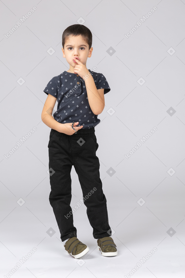 Front view of a cute boy touching mouth with finger