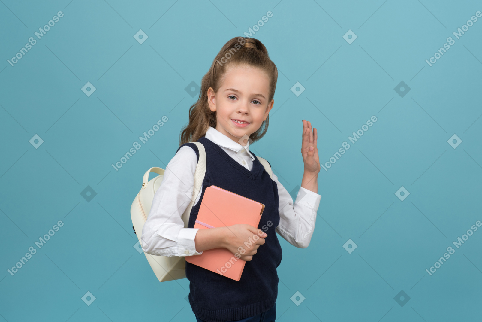 Smiling litlle schoolgirl holding a book and waving