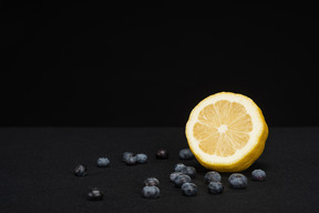 Zitrone, die im schwarzen hintergrund mit blaubeeren liegt