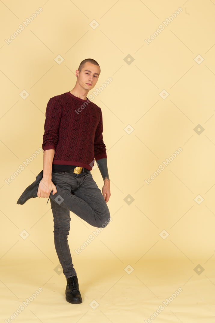 Вид в три четверти уставшего молодого человека в красном пуловере, касающегося его лодыжки