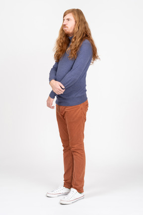 Side view of a young man in casual clothes standing with crossed arms