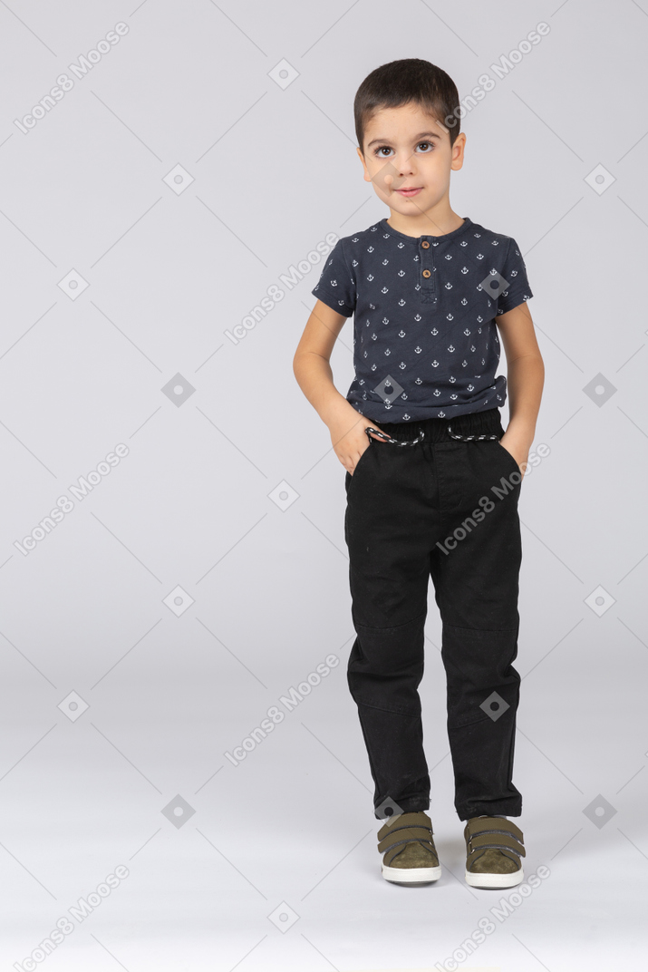 Front view of a cute boy standing with hands in pockets and looking at camera