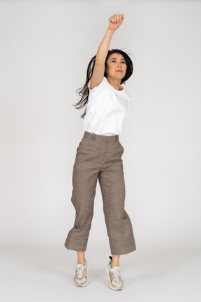 Front view of a jumping young lady in breeches and t-shirt outstretching her hand