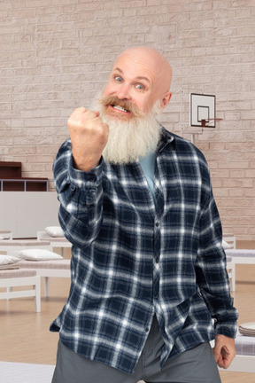 Old man showing off fist standing in basketball court with beds