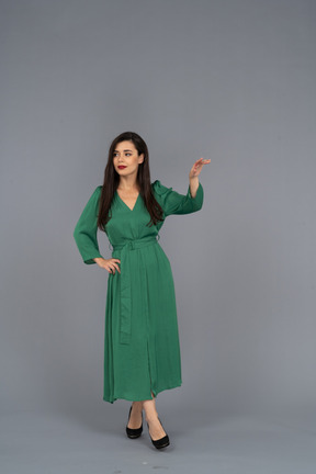 Вид спереди молодой леди в зеленом платье, поднимающей руку