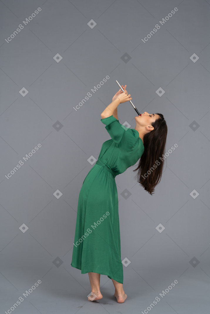 Vista lateral de una señorita en vestido verde tocando la flauta mientras se inclina hacia atrás