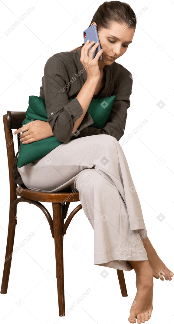 Vista frontal de una mujer joven sentada en una silla mientras tiene una llamada telefónica