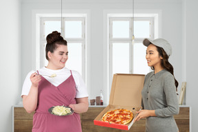 Una mujer de talla grande con un plato de ensalada, saludando a una repartidora que le trajo una caja de pizza