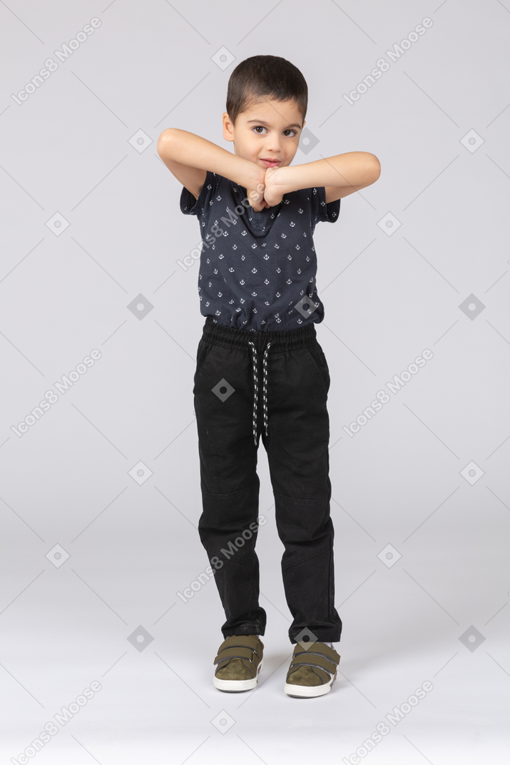 Vista frontal de um lindo menino posando com as mãos na frente do peito e olhando para a câmera