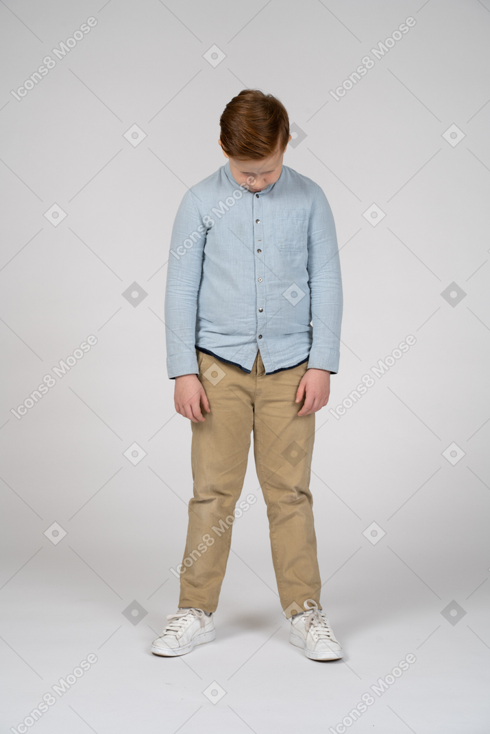 Vista frontal de um menino em roupas casuais, abaixando a cabeça