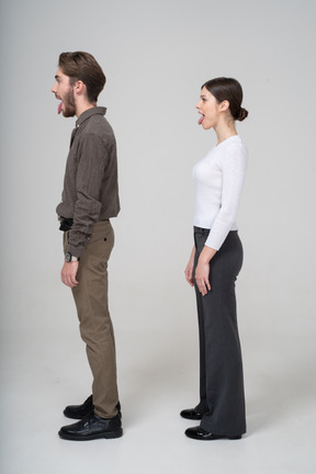 Side view of a crazy young couple in office clothing showing tongue