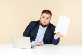 Giovane uomo in sovrappeso seduto alla scrivania e in possesso di cornice