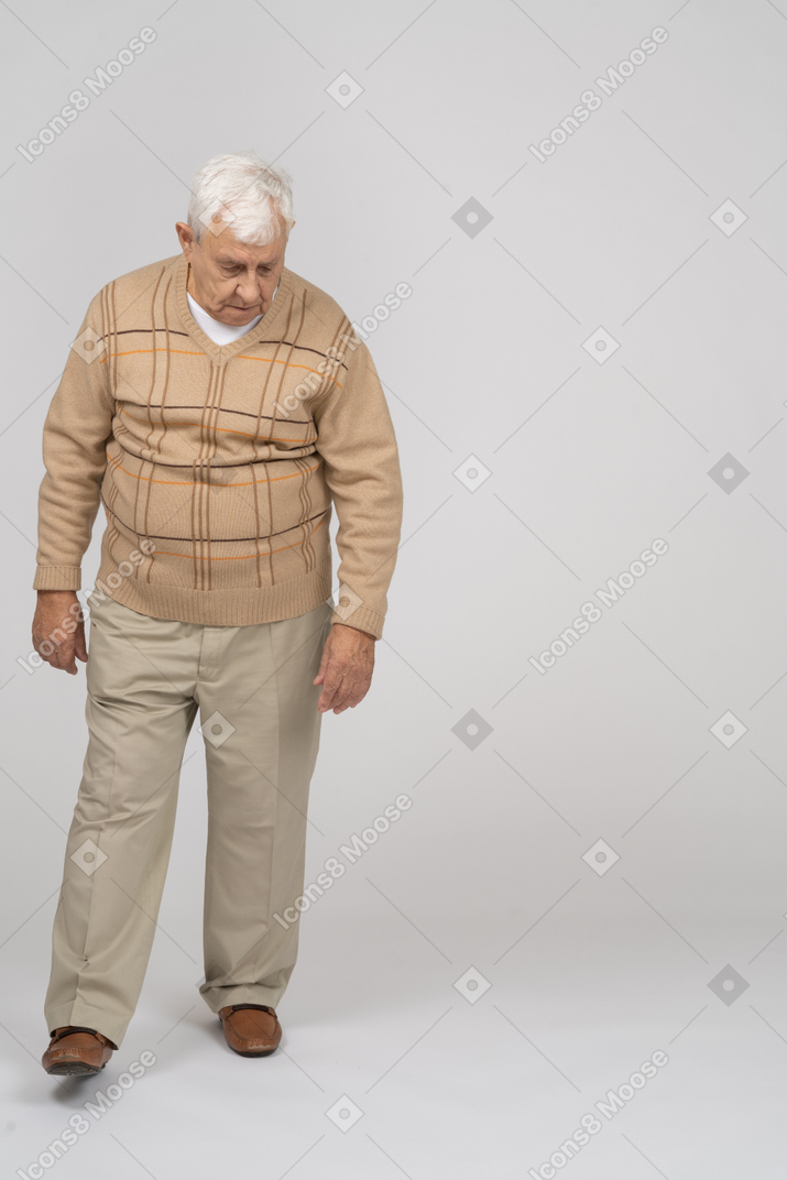 Vue de face d'un vieil homme en vêtements décontractés marchant et regardant vers le bas