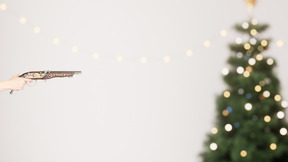 A person holding a gun in front of a christmas tree