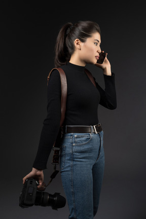 Young woman with camera speaking by phone