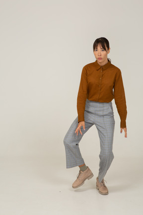 Front view of a dancing young asian female in breeches and blouse bending knees