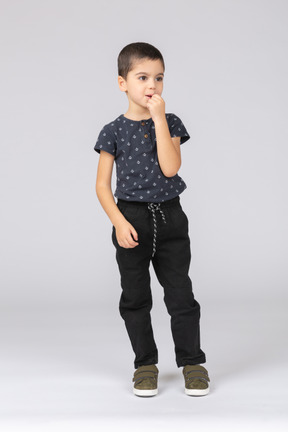 Вид спереди симпатичного мальчика в повседневной одежде, засовывающего пальцы в рот