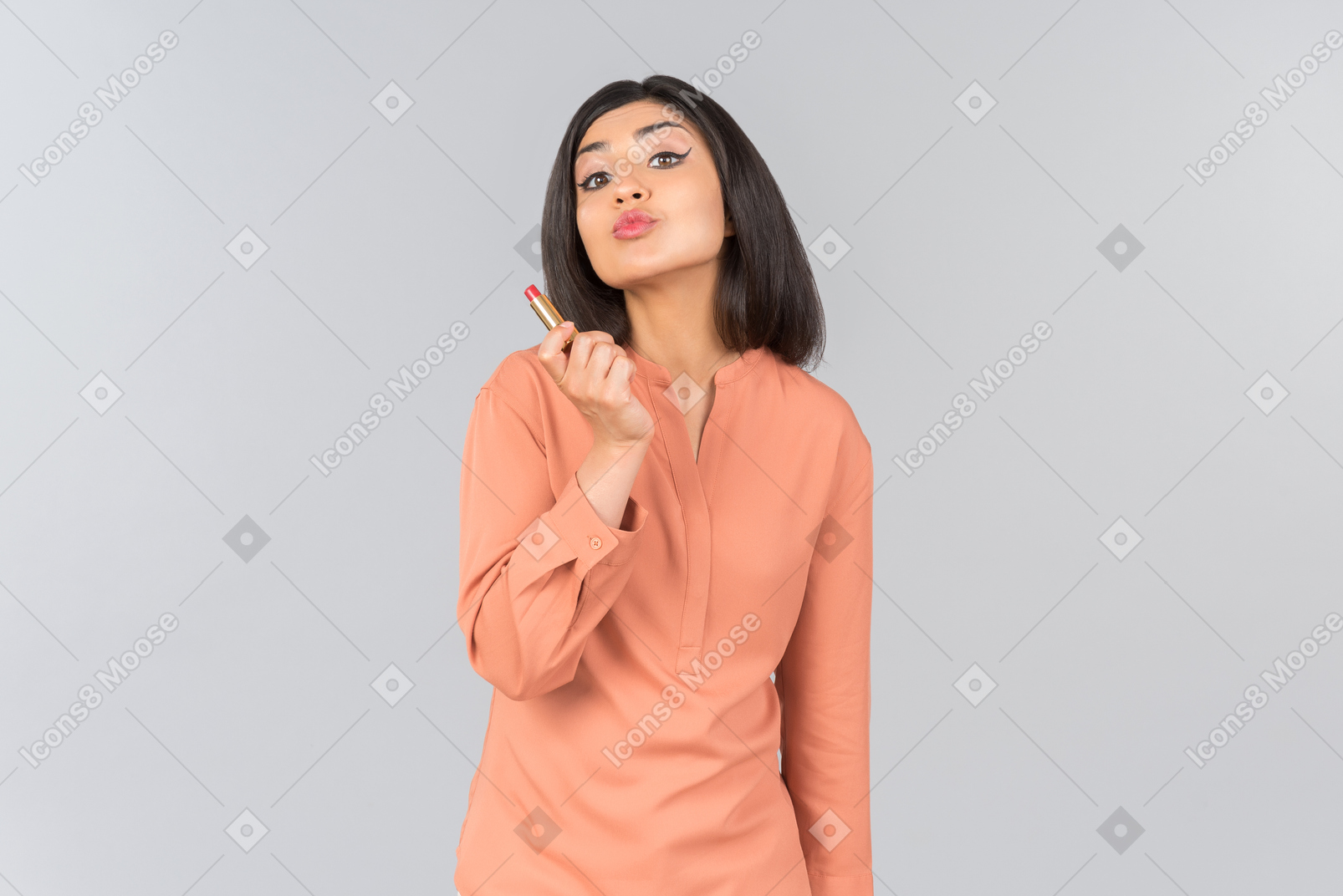 Indian woman in orange top holding lip balm and sending air kiss