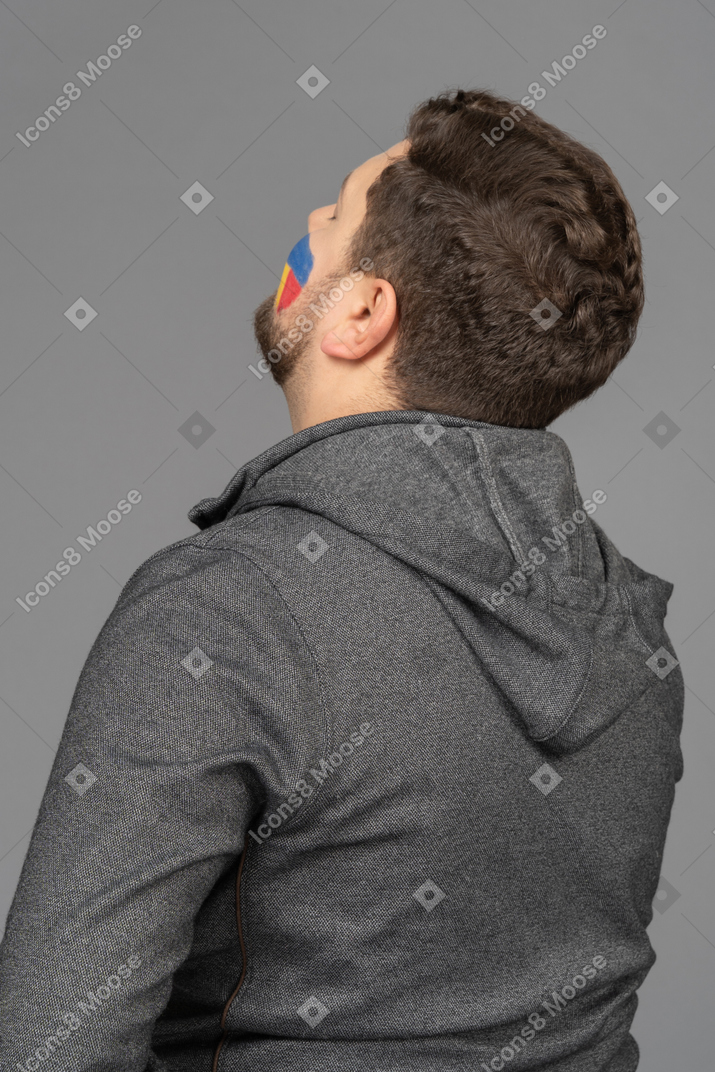 Three-quarter back view of a tired male football fan with colorful face art