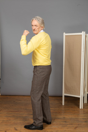 Vista lateral de un anciano mirando a la cámara mientras demuestra su fuerza
