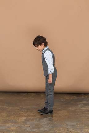 Vue latérale d'un garçon mignon en costume gris regardant vers le bas