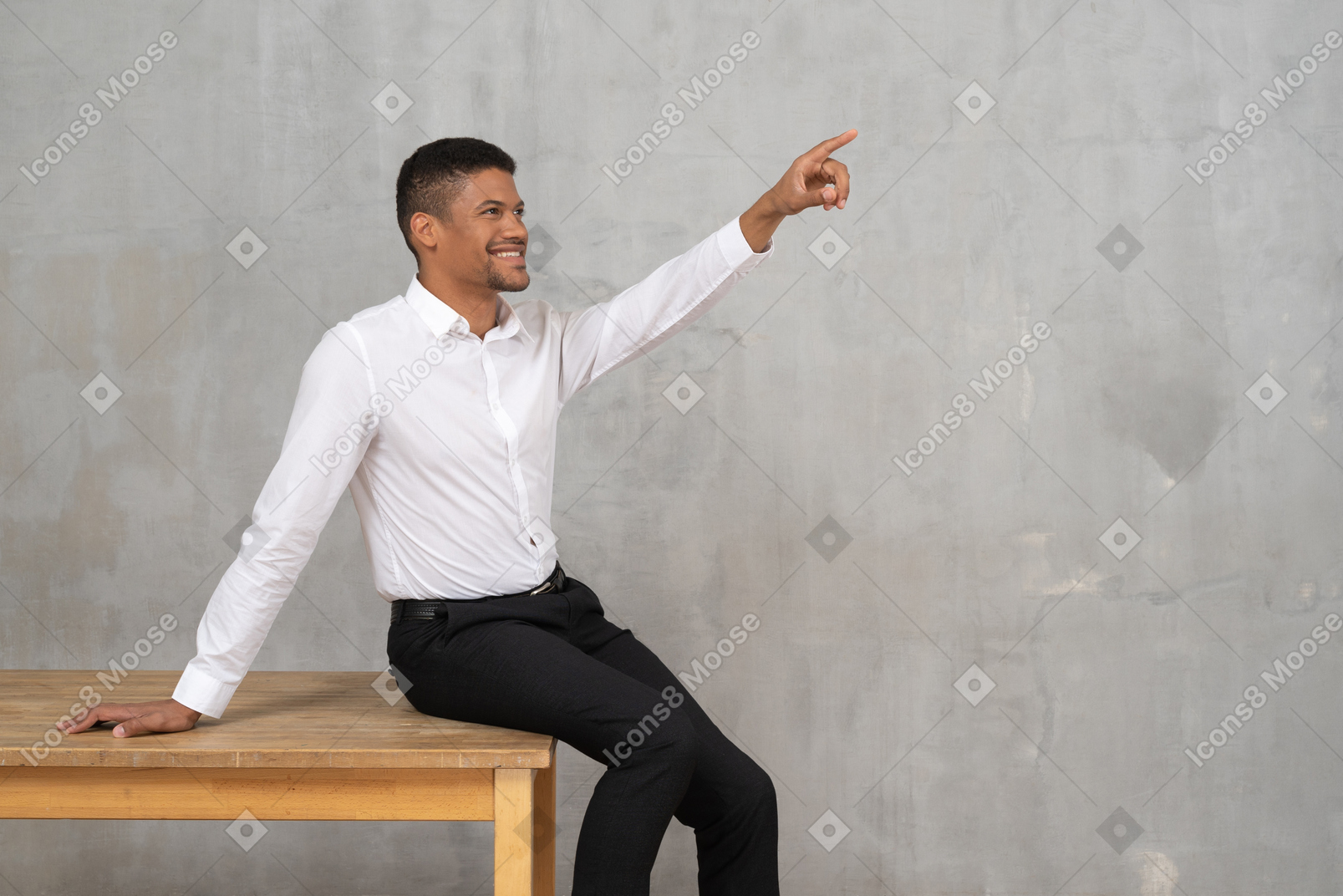 Smiling man in office clothes sitting on a table and pointing up