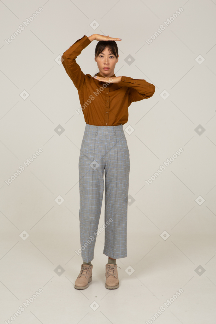 Vista frontal de uma jovem mulher asiática de calça e blusa mostrando o tamanho da cabeça